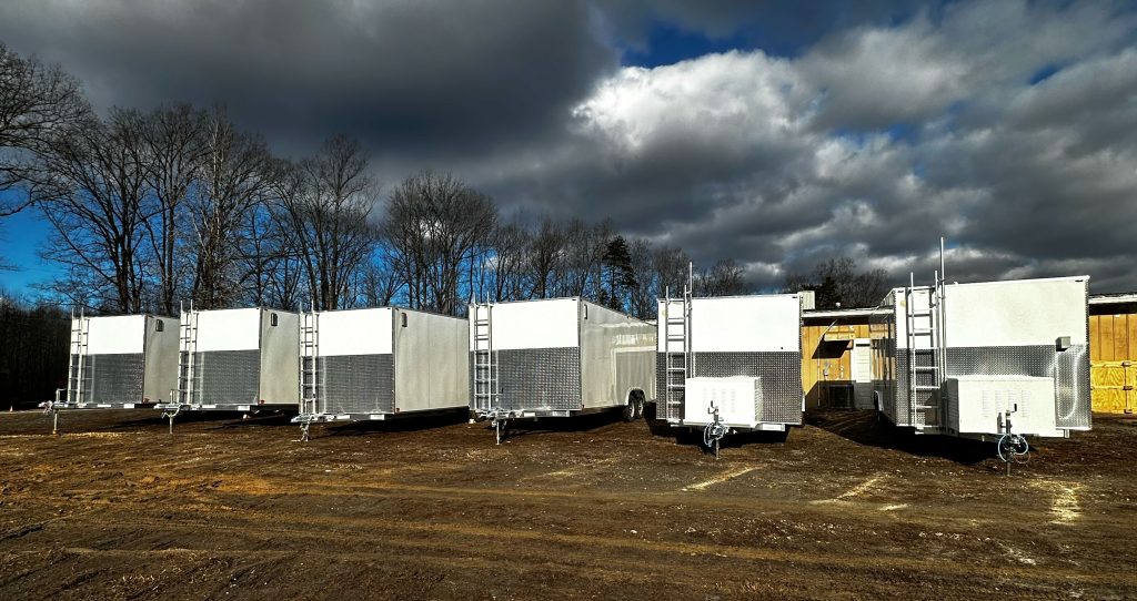 A group of custom trailers in a field beneath a cloudy sky, showcasing various trailer solutions